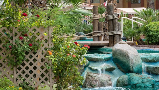A garden with a wooden fence, a small waterfall, and a pool. - Westgate Flamingo Bay Resort (Las Vegas)