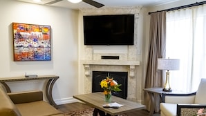 A living room with a fireplace, a flat-screen TV, a painting, and a coffee table with a vase of flowers. - Westgate Flamingo Bay Resort (Las Vegas)