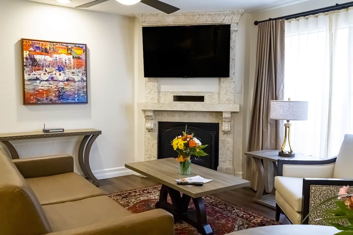 A living room with a fireplace, a flat-screen TV, a painting, and a coffee table with a vase of flowers.