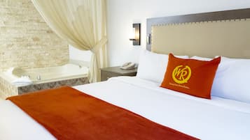 Een hotelkamer met een groot bed, een hoofdbord met een logo, een nachtkastje met een telefoon, een wandlamp en een bad.