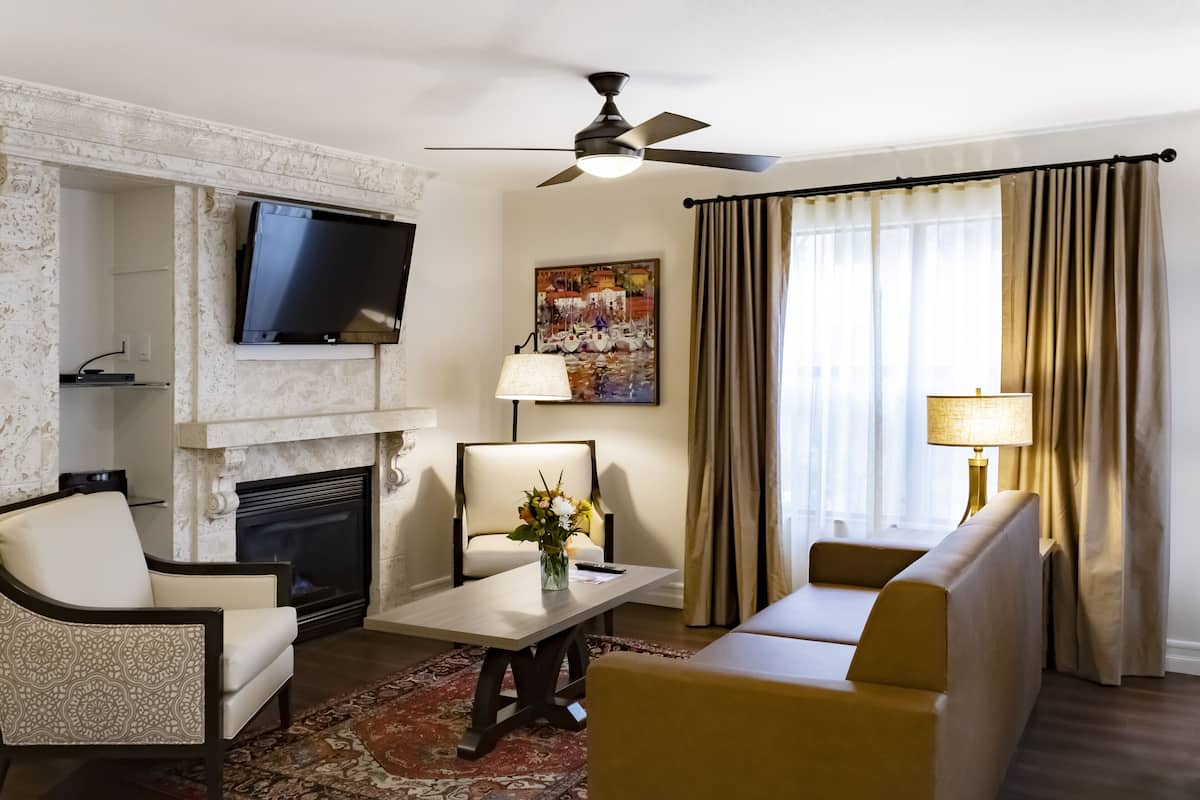 A living room with a fireplace, a flat-screen TV mounted above it, a sofa, a coffee table with a vase of flowers, and a ceiling fan.