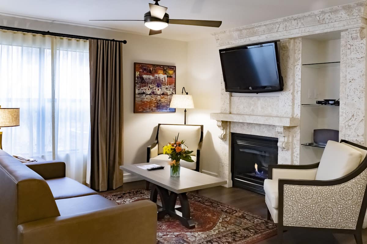 A living room with a sofa, armchair, table with a vase, a fireplace, and a TV mounted on the wall.