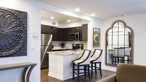 A modern kitchen with dark cabinetry, a stainless steel refrigerator, and a microwave. There is a small island with two chairs and a coffee maker. - Westgate Flamingo Bay Resort (Las Vegas)