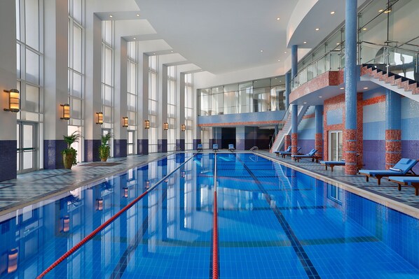 Relax by the pool surrounded by glass walls and a staircase, with lounge chairs and a seating area nearby.