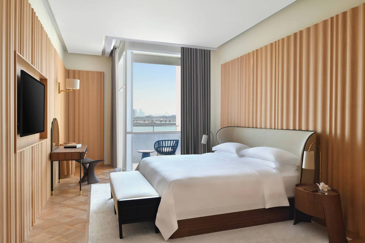 A modern hotel room with a large bed, a desk, a chair, and a television.