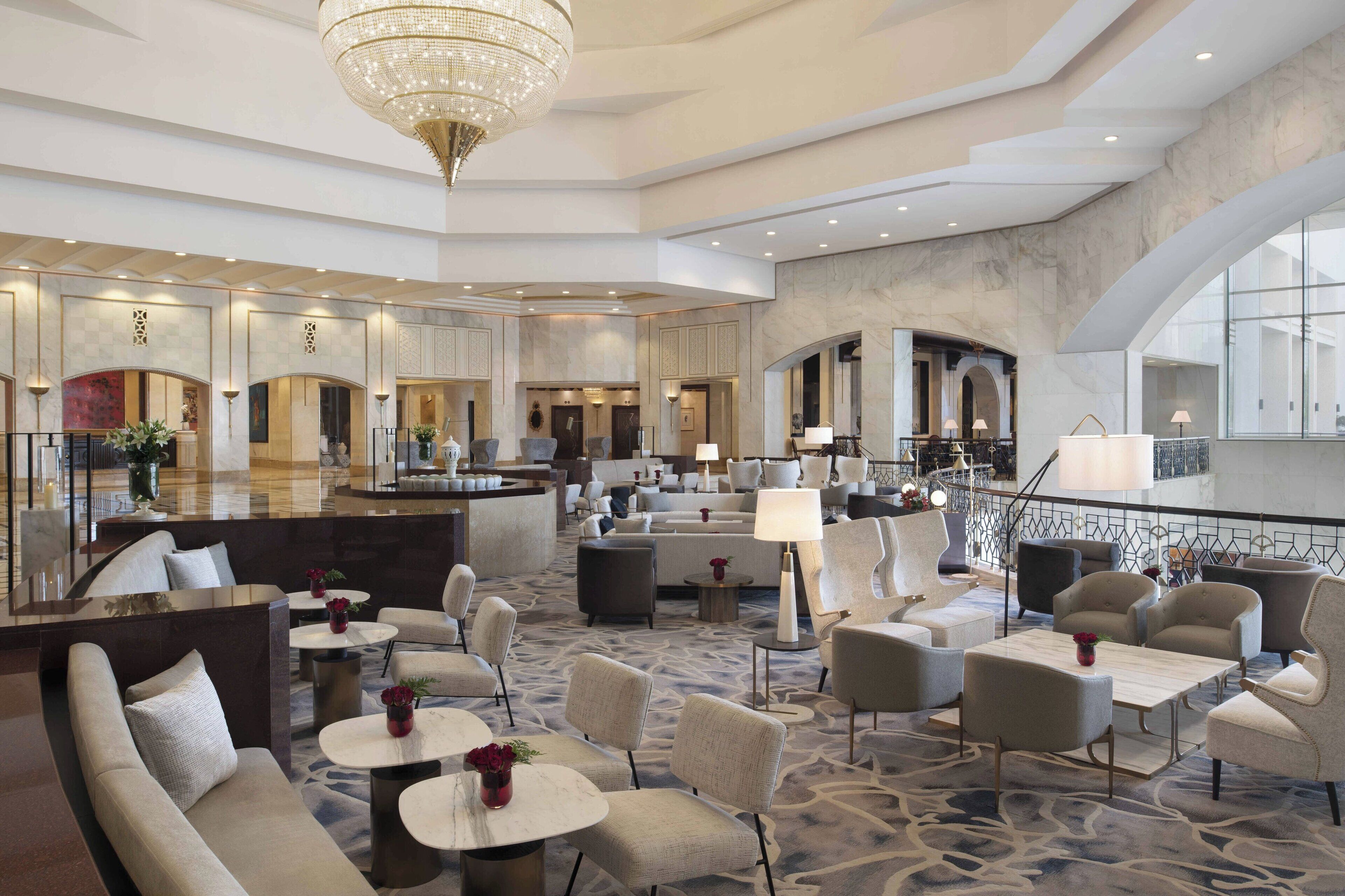A spacious lobby with a high ceiling, a chandelier, and a mix of seating areas including sofas and chairs.