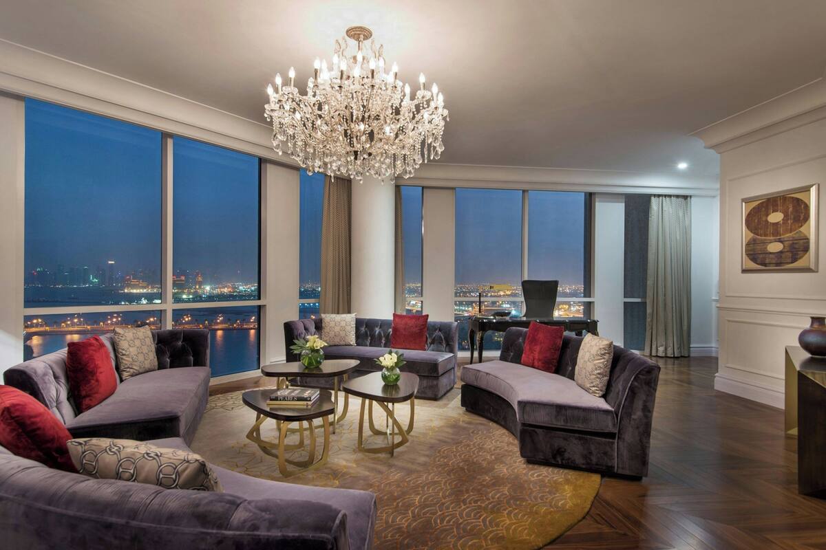 A spacious living room with a large chandelier, multiple sofas, and a view of a cityscape at night.