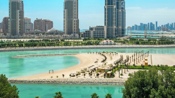 Un paisaje urbano costero con rascacielos, una playa con palmeras y un cielo azul despejado.