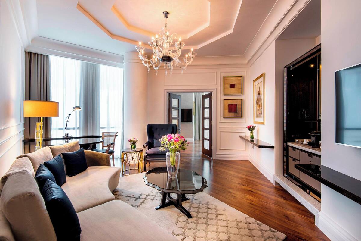 A modern living room with a sofa, a glass coffee table, a chandelier, and a flat-screen TV.