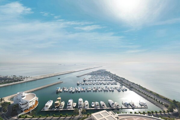 A marina with numerous boats docked, a large building with a curved roof, and a clear sky.