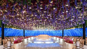 Un espacio para eventos amplio y elegantemente decorado, con un escenario central rodeado de filas de sillas y arreglos florales.