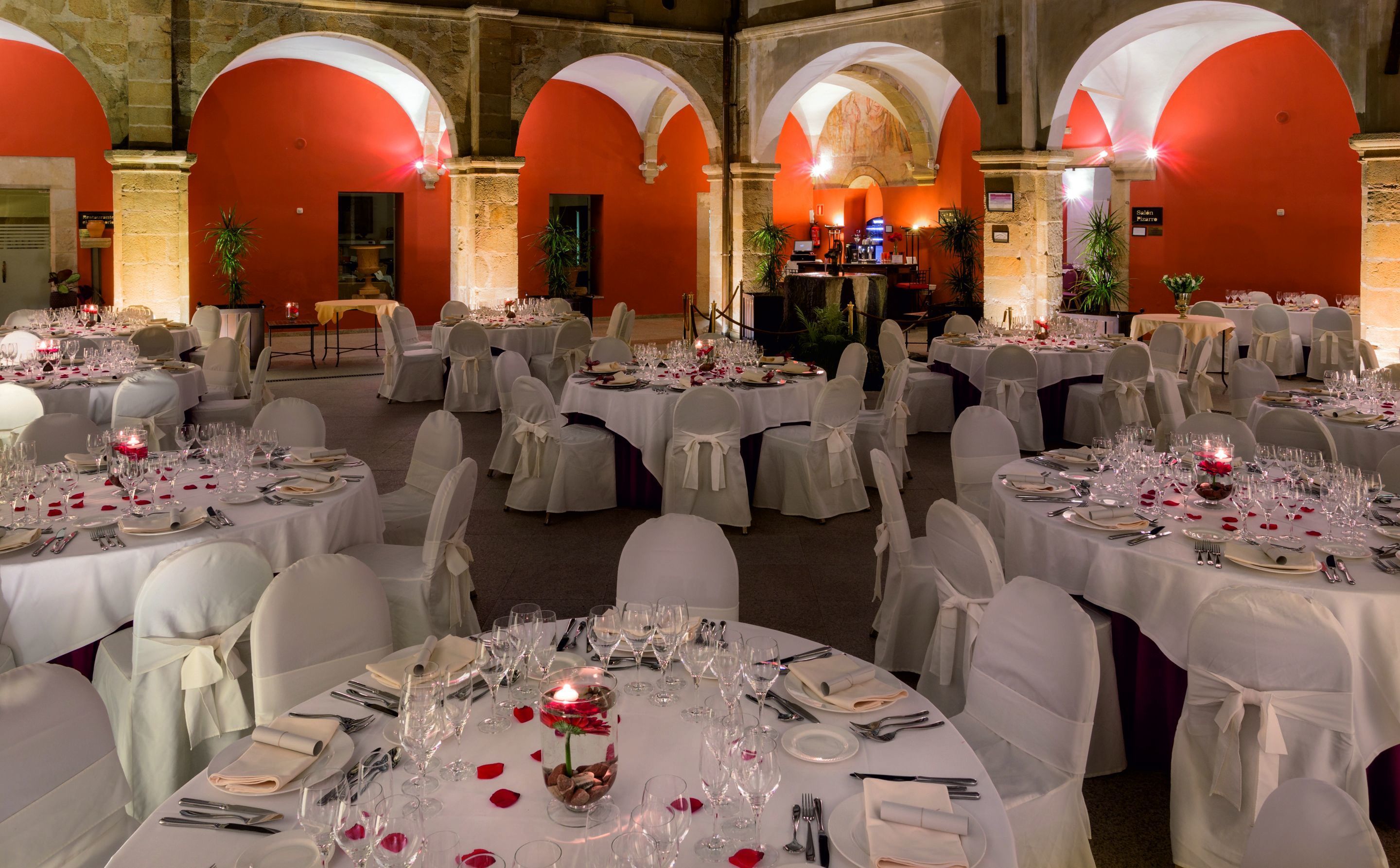 A banquet hall with round tables set for a formal event, featuring white tablecloths, glassware, and chairs with white sashes.
