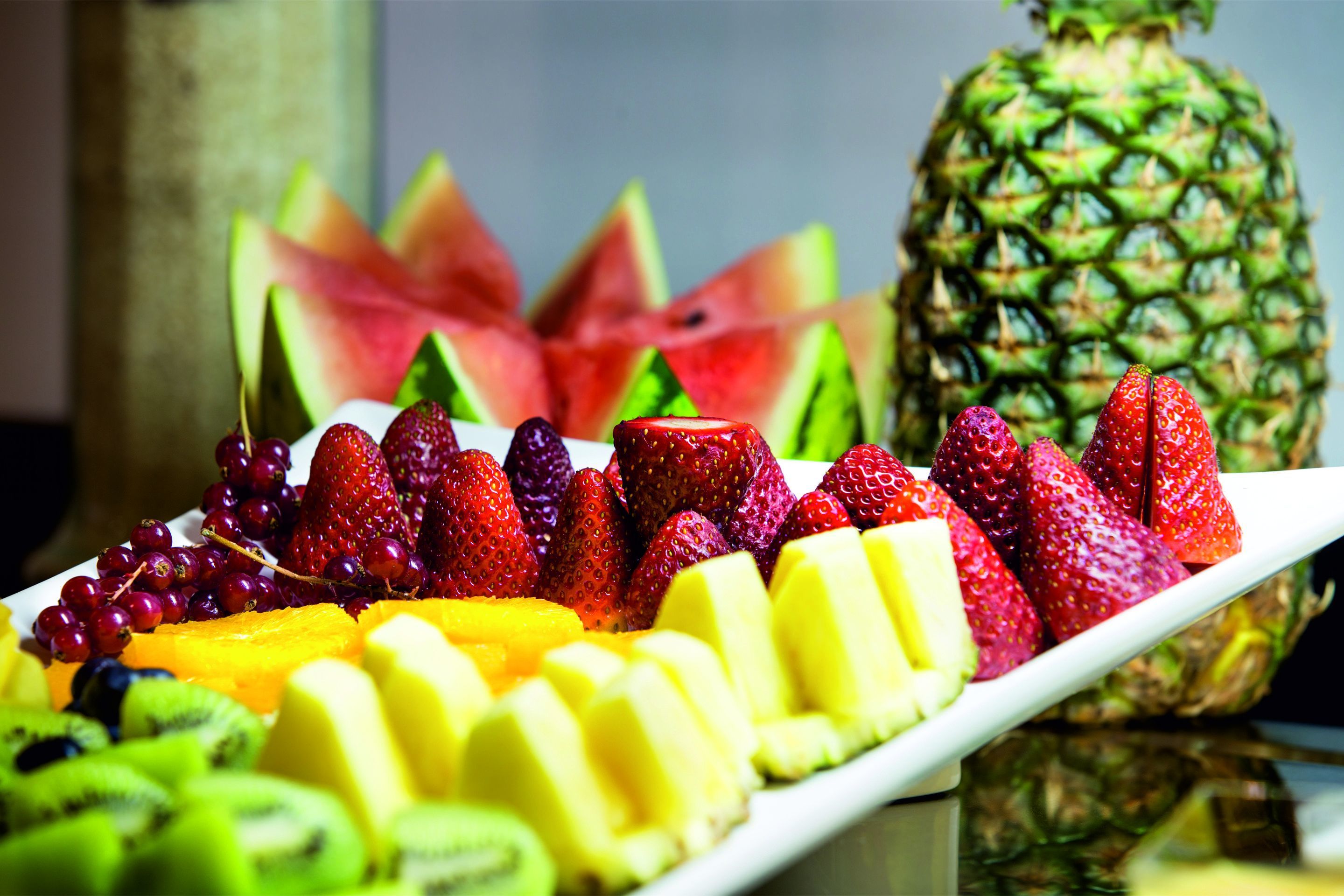 Une variété de fruits, notamment des fraises, des raisins, des kiwis et des ananas, disposés sur une assiette blanche.