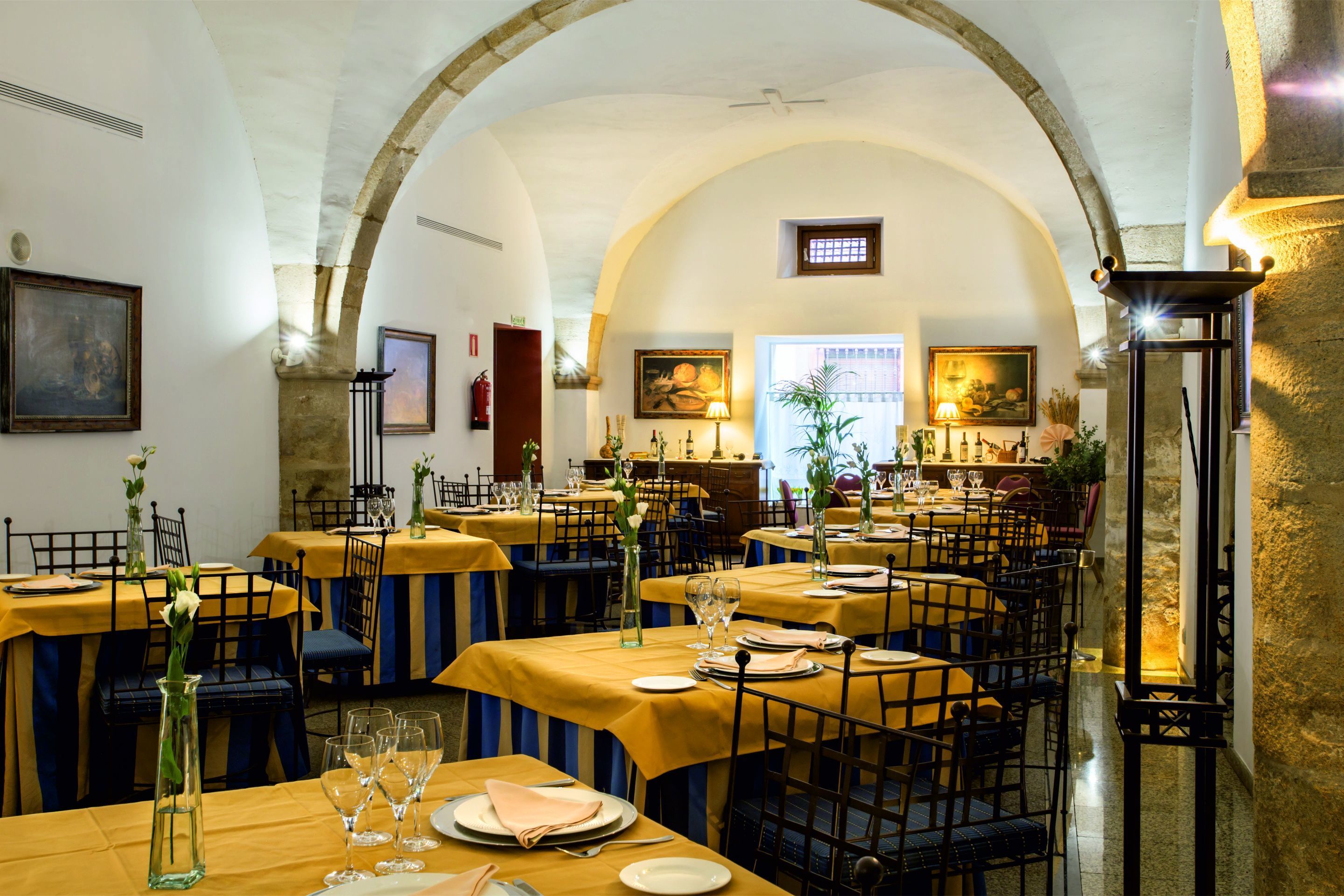 A restaurant with tables set for dining, featuring yellow tablecloths and blue chairs.