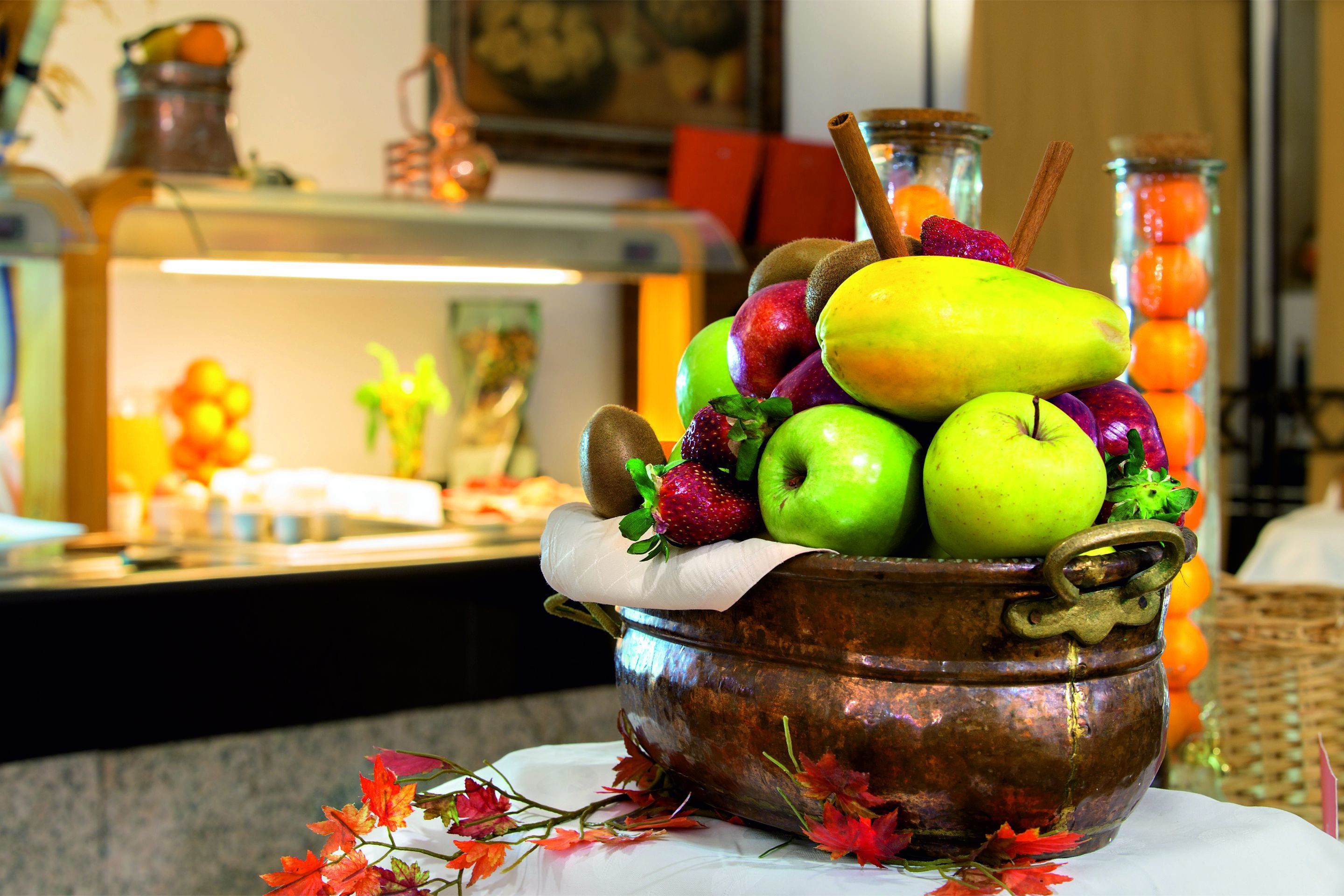 A copper pot filled with fruits and a cinnamon stick on a table with autumn leaves.