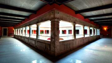 Un interior espacioso con un área central abierta enmarcada por columnas, un techo alto y una pared roja.