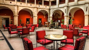 Un amplio patio con asientos y mesas rojas, arcos de piedra y plantas en macetas.