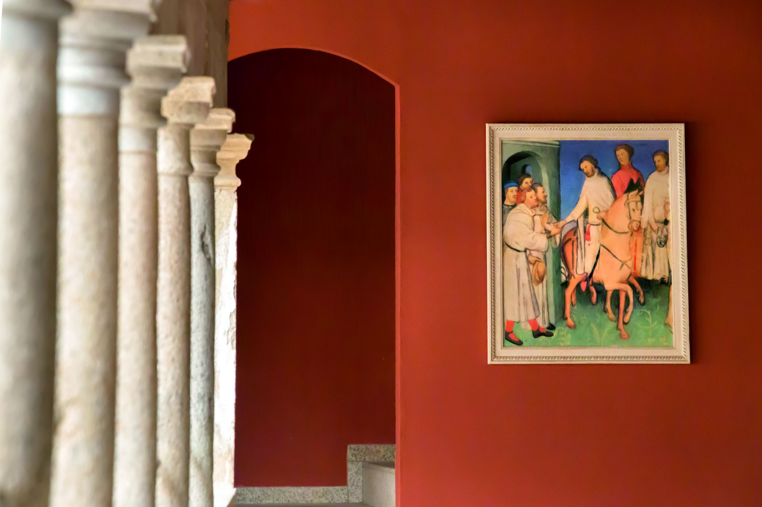 A framed painting of a historical scene on a red wall.