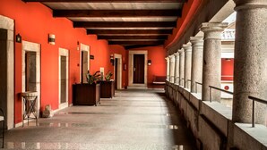 Un pasillo con paredes rojas, columnas de piedra y piso de baldosas.