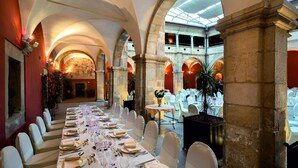 Un salón de banquetes con una larga mesa dispuesta para un evento formal, techos abovedados y vistas al nivel superior.