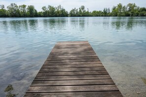 A wooden dock extending into calm water with a forested shoreline in the background. - Hotel Langwieder See (Munich)