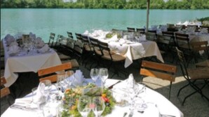 An outdoor dining area with tables set for a meal, overlooking a body of water. - Hotel Langwieder See (Munich)