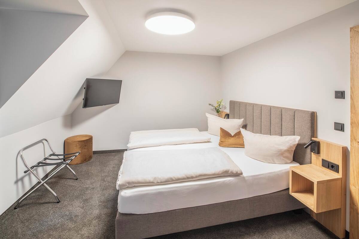 Un dormitorio moderno con cama, mesita de noche y televisor montado.