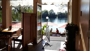 An open doorway leading to a terrace with a view of a lake and outdoor seating. - Hotel Langwieder See (Munich)