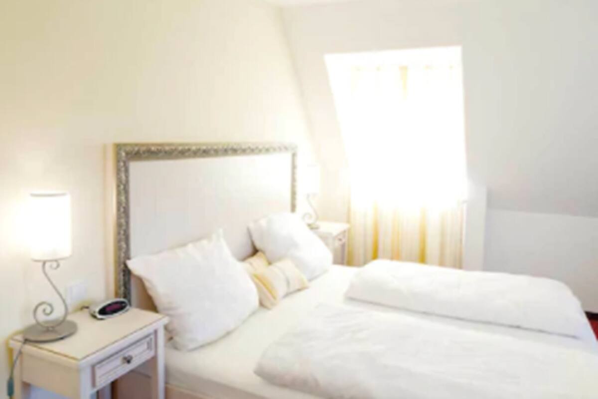 Una habitación de hotel con una cama, una mesita de noche con lámpara y una ventana con cortinas.