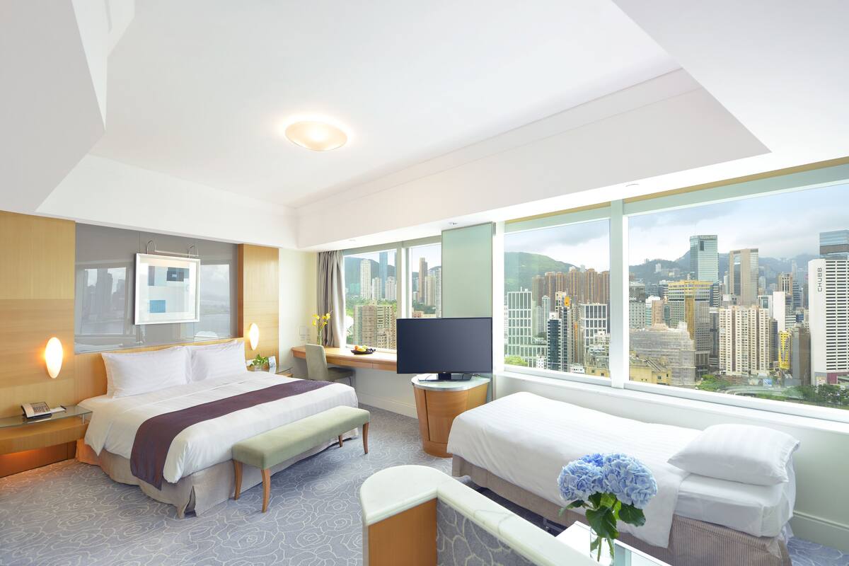 Une chambre d’hôtel moderne dotée d’un grand lit, d’un bureau avec un ordinateur, d’un petit canapé et d’une grande fenêtre donnant sur la ville.