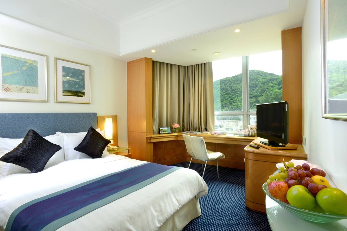 Une chambre d’hôtel équipée d’un lit, d’un bureau, d’une chaise, d’une télévision et d’un panier de fruits.