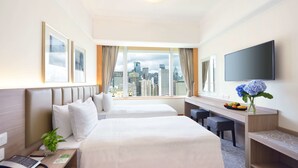 Een hotelkamer met twee bedden, een bureau, een televisie en uitzicht op de stad.