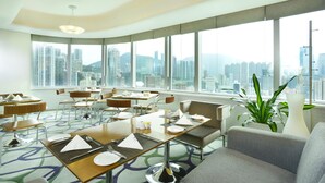 Een modern restaurantgedeelte van een hotel met gedekte tafels, grote ramen met uitzicht over de stad en strakke inrichting.