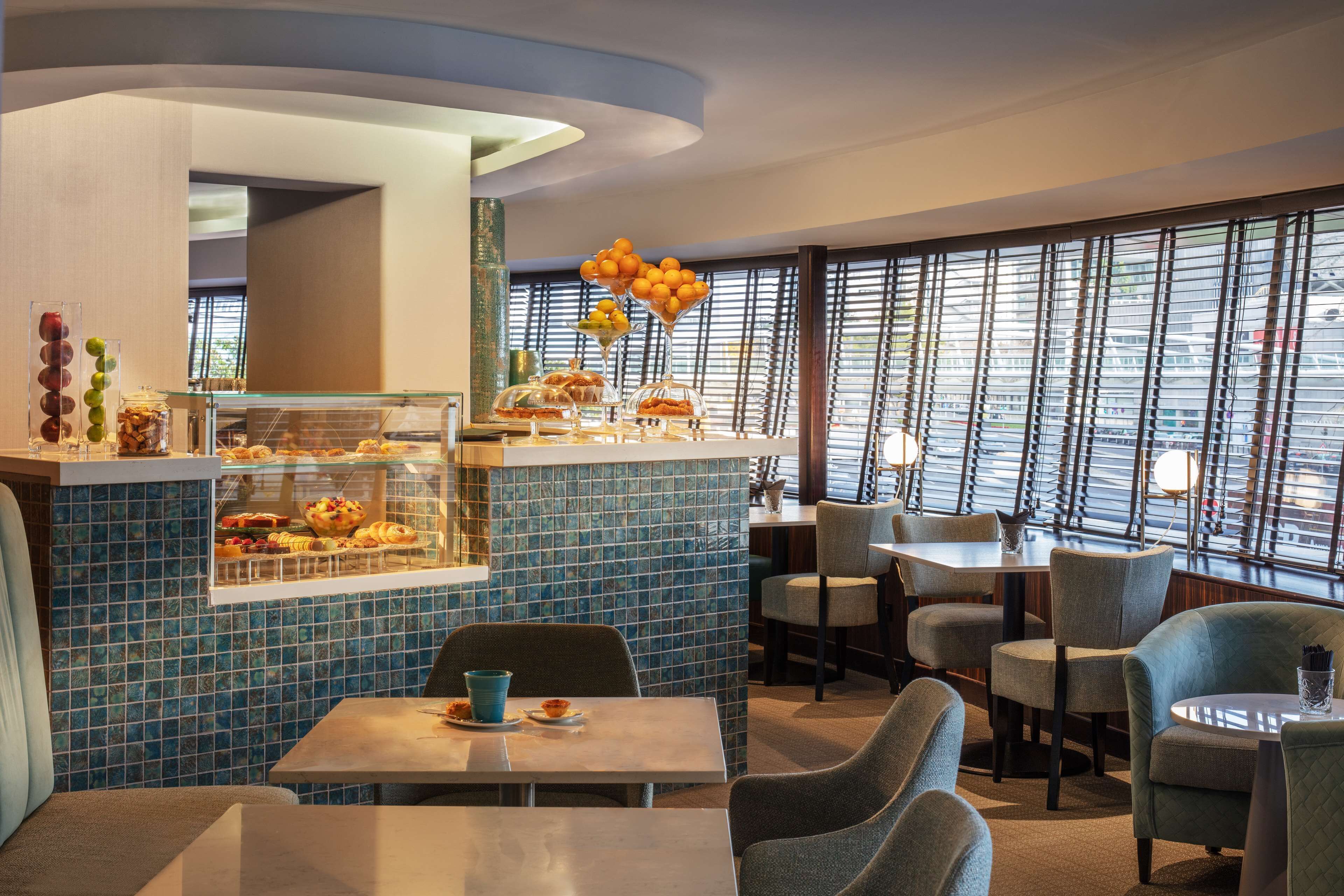 Un restaurant avec un mur recouvert de carreaux bleus, une vitrine où sont exposées des pâtisseries, et une vue dégagée grâce à de grandes fenêtres.
