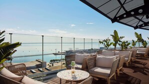 Terraza en la azotea con mobiliario de mimbre, una mesa redonda con una botella y vistas al mar y un puente.