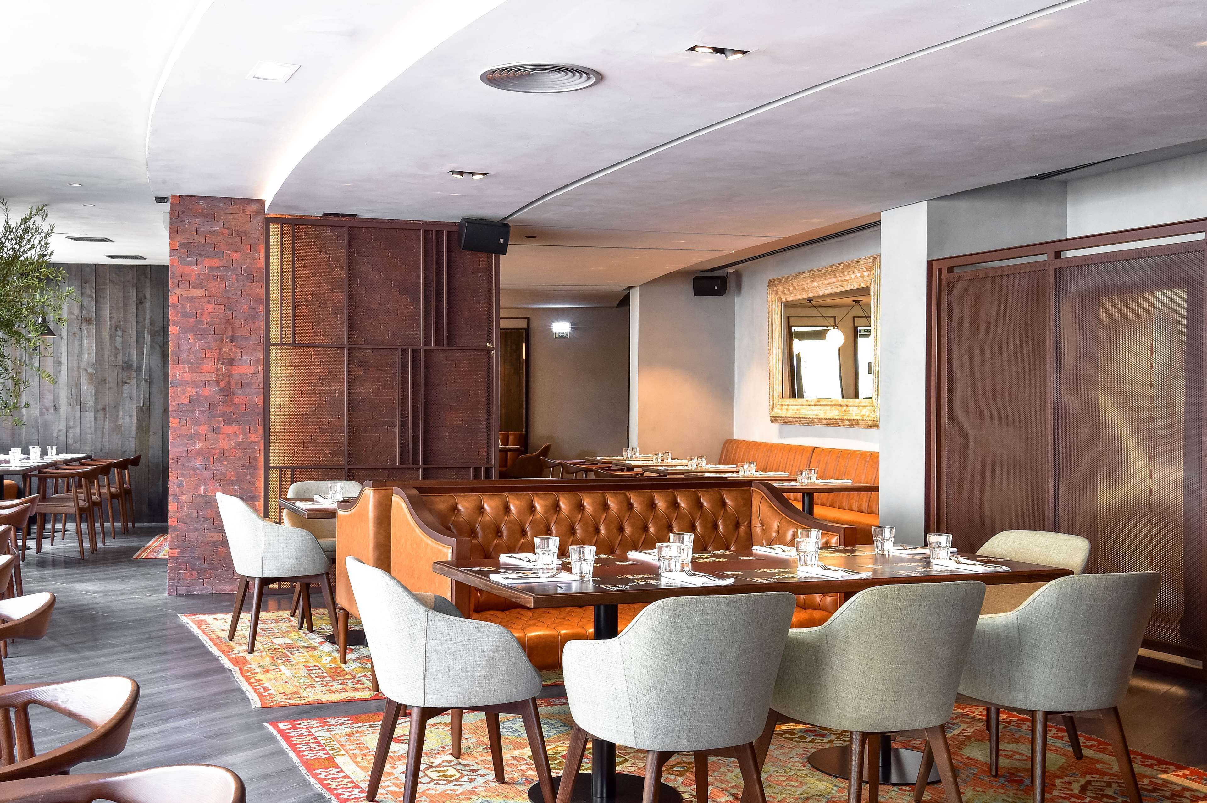 A restaurant with a high ceiling, exposed brick walls, and a mix of seating including tables and a booth.