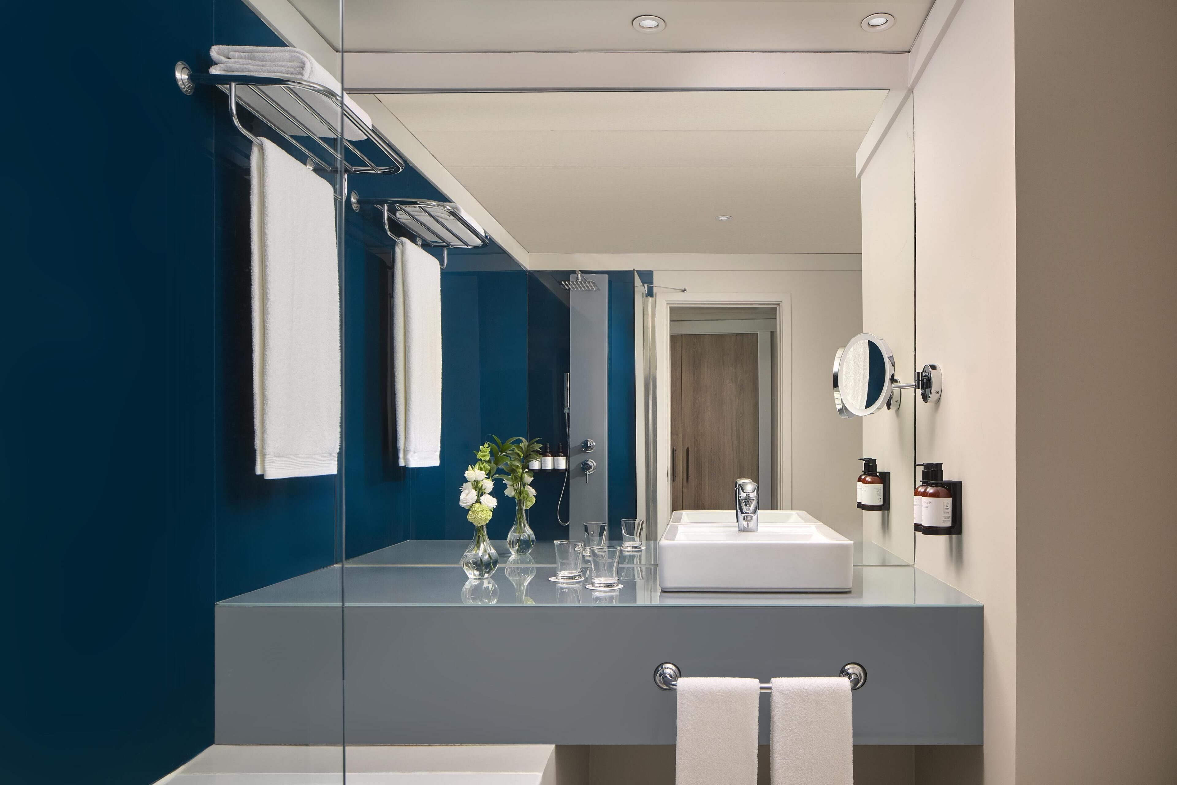 A modern bathroom with a large mirror, a white sink, and a glass shower enclosure.