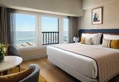 A hotel room with a large bed, a dining table, and a view of the sea.