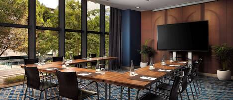 A conference room with large windows, a flat-screen TV, and a blue patterned carpet.