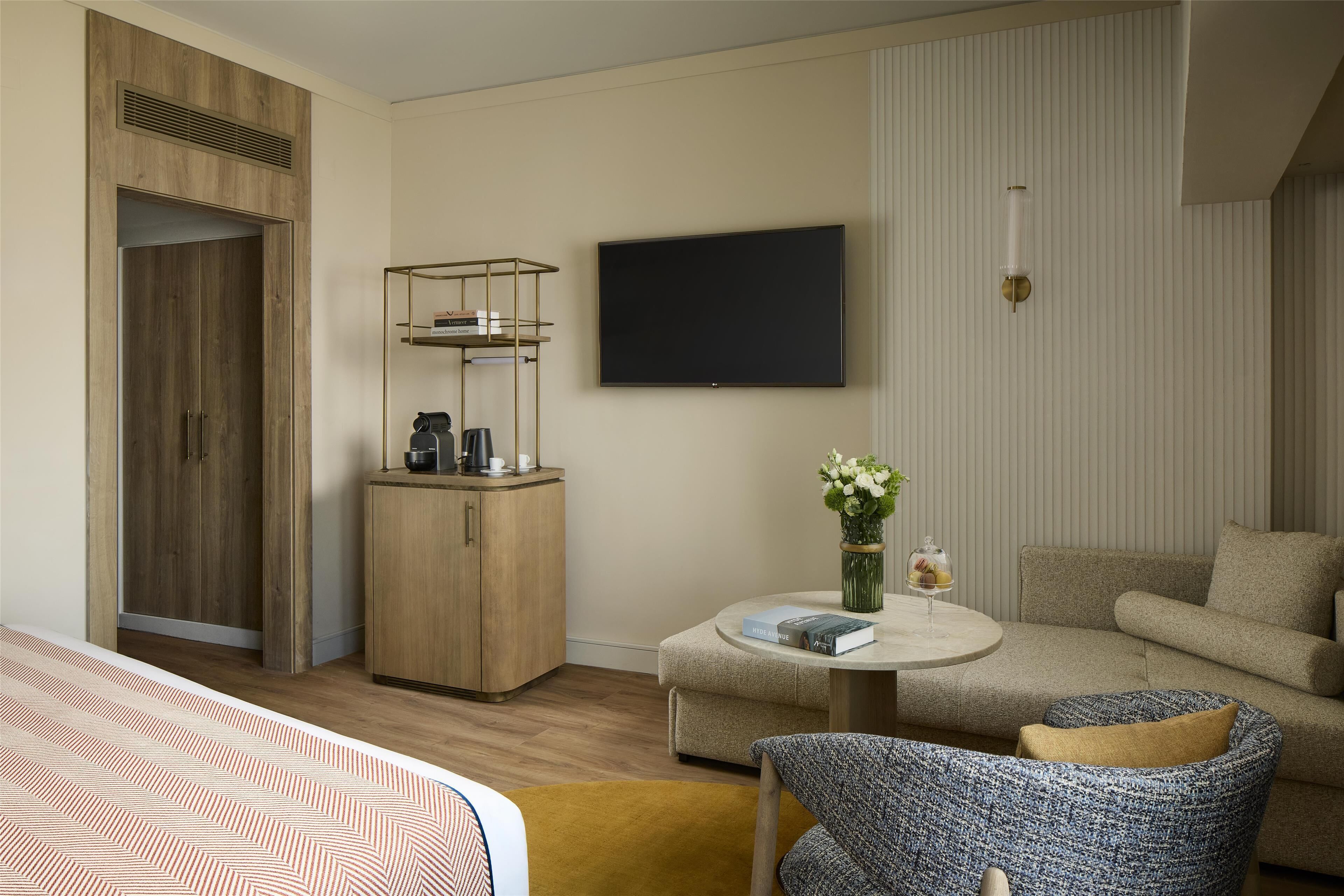Habitación de hotel con cama, sofá, mesa de centro, televisor, armario y un mueble pequeño.