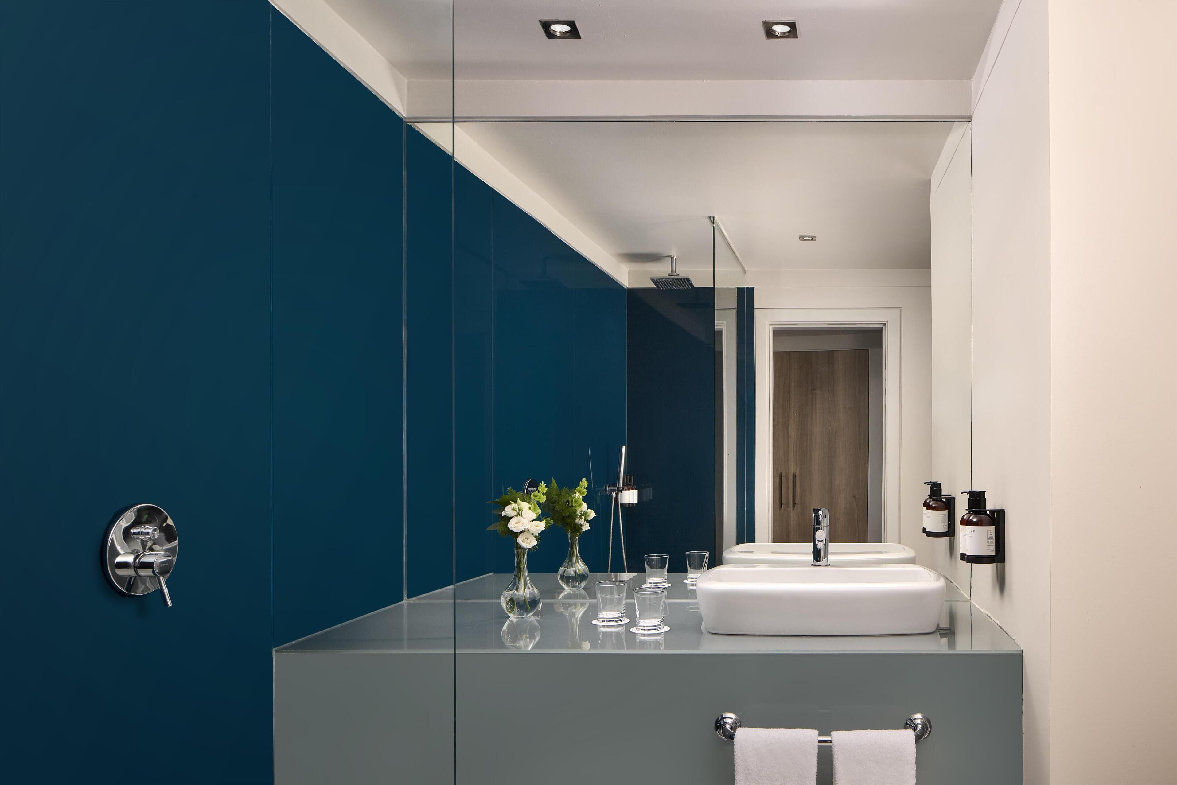 A modern bathroom with a large mirror, a white sink, and a blue accent wall.