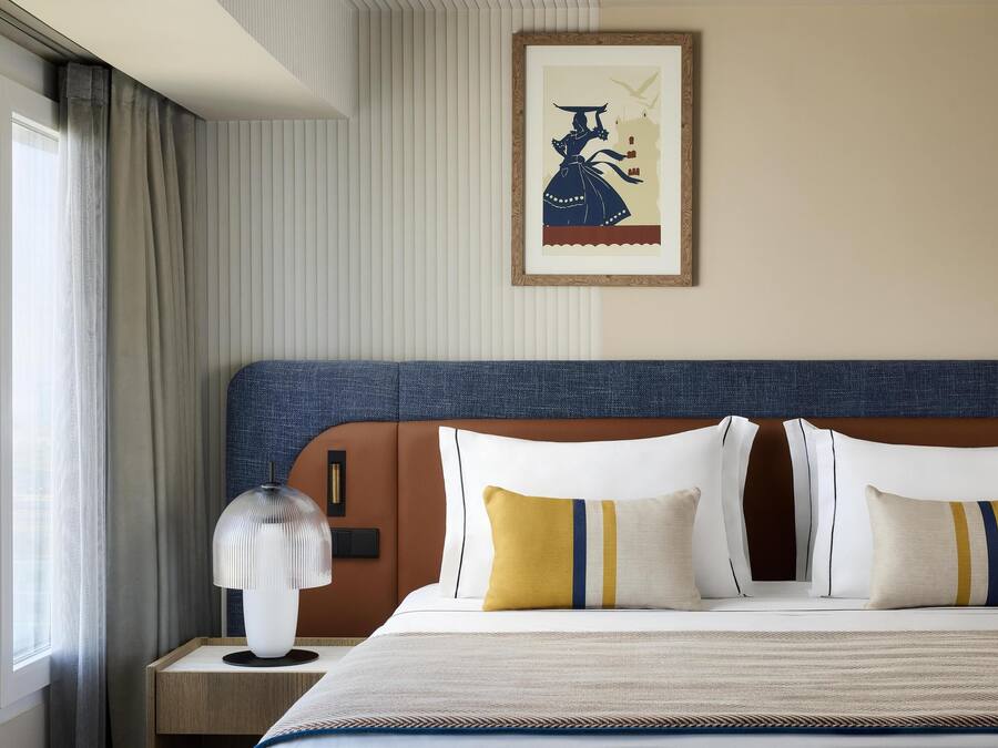 A neatly made bed with a blue headboard, white and yellow pillows, and a striped bedspread.