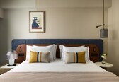 A hotel room with a large bed, a nightstand with a lamp, a framed picture on the wall, and a small table with a vase of flowers.