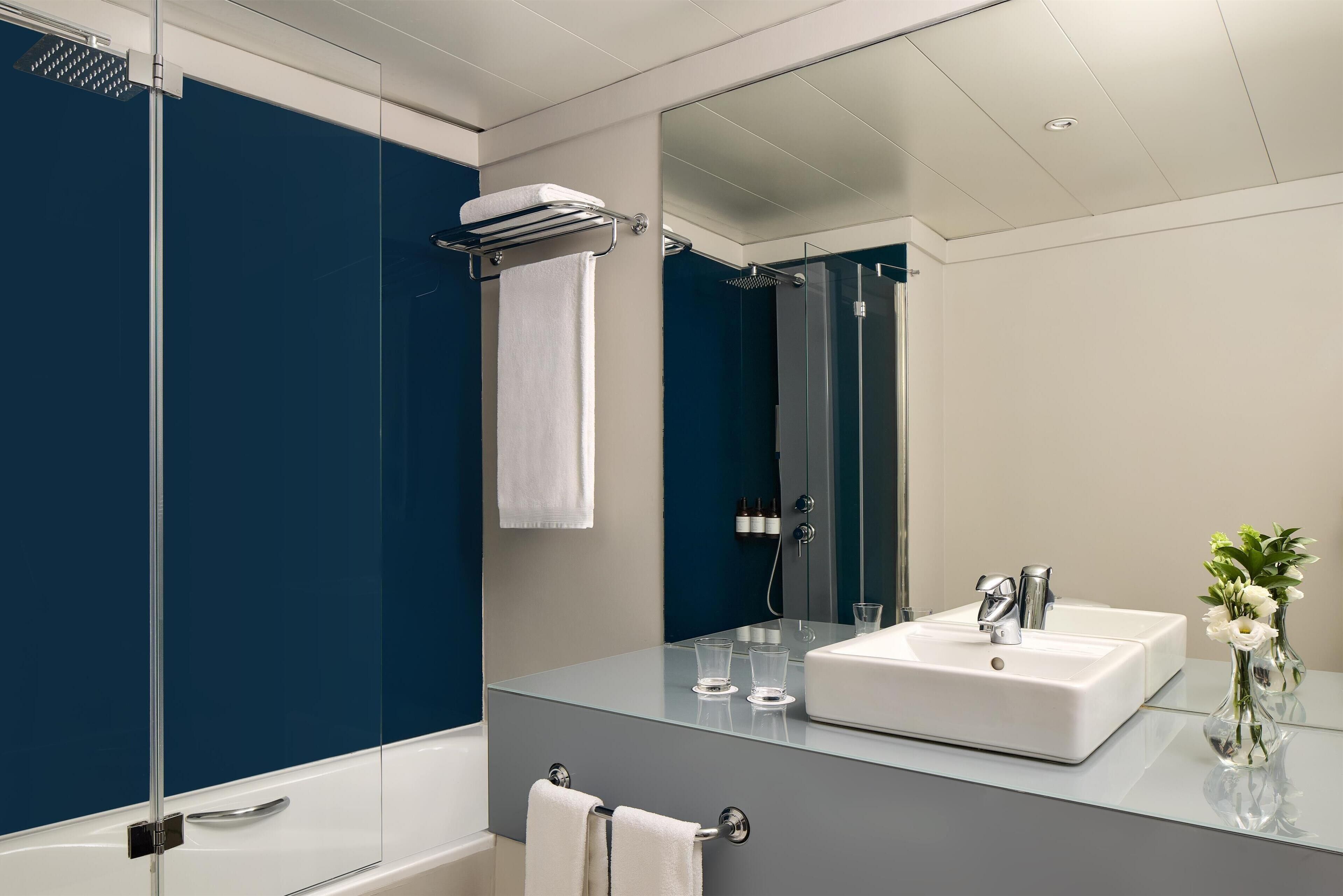 A modern bathroom with a glass shower enclosure, a white bathtub, a large mirror, and a white sink with two faucets.