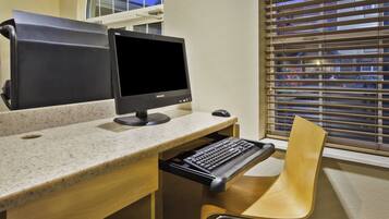A workspace with a desktop computer, a keyboard tray, a chair, and a window with blinds.