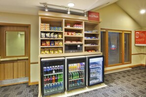 A snack and beverage area with shelves stocked with chips, a microwave, and refrigerators containing various drinks. - TownePlace Suites Detroit Sterling Heights (Sterling Heights)