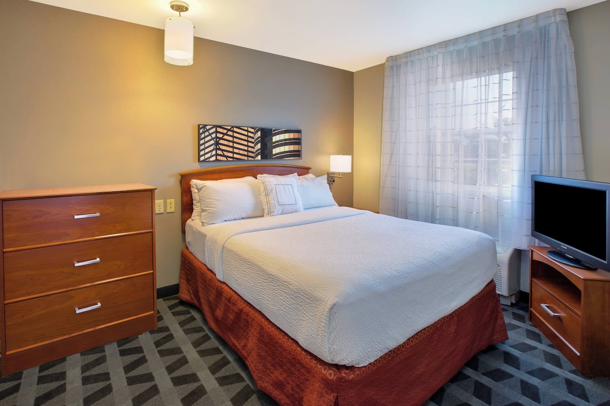 A hotel room with a bed, a TV, a dresser, and a wall-mounted artwork.