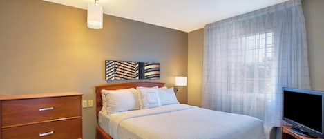 A hotel room with a bed, a TV, a dresser, and a wall-mounted artwork.