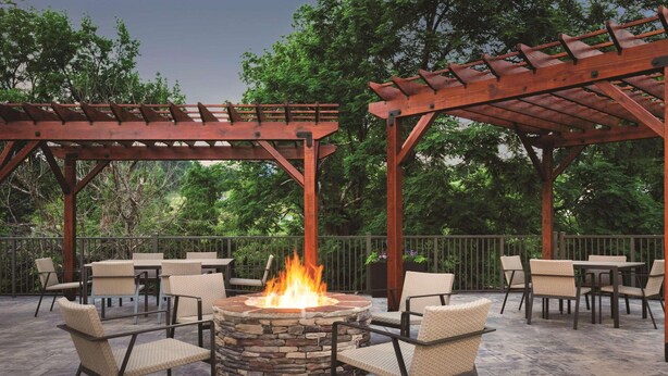 An outdoor patio area with a stone fire pit surrounded by wicker chairs and tables, under wooden pergolas. - Country Inn & Suites by Radisson, Pigeon Forge South, TN (Pigeon Forge)