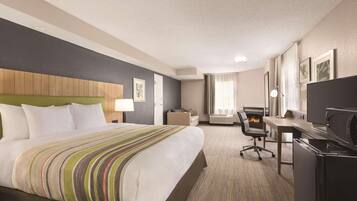 A hotel room with a bed, a desk, a chair, a TV, and a fireplace.